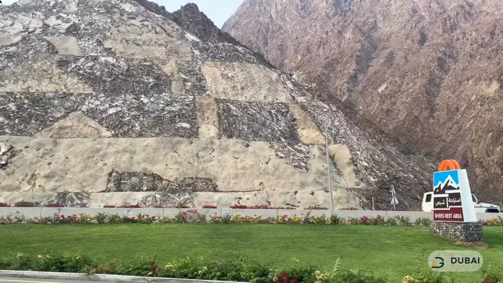 Shees Rest Area entrance sign with landscaped gardens and Hajar mountains